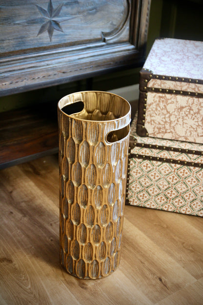 Textured gold umbrella stand styled beside antique furniture and decorative storage boxes.